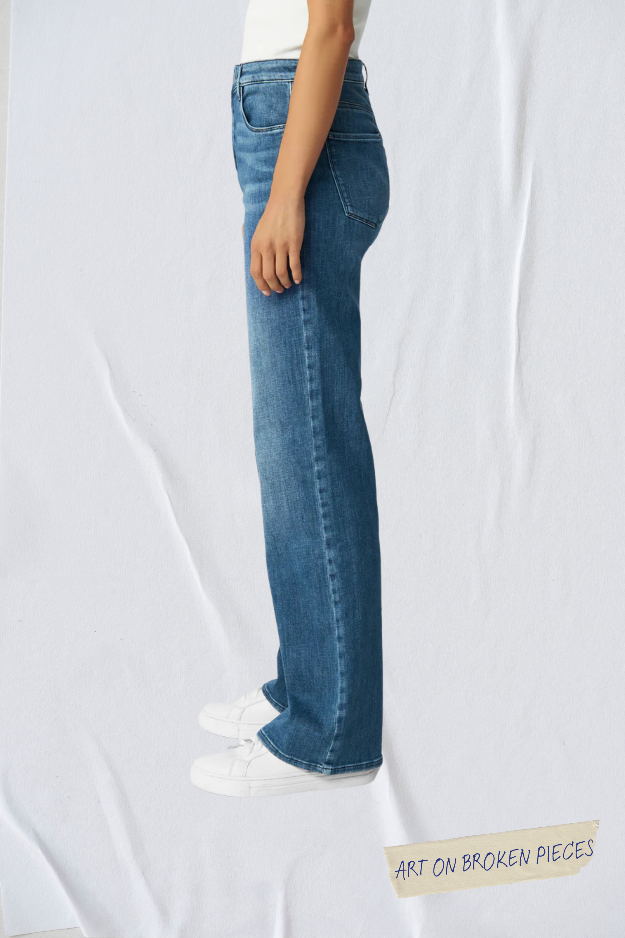 Seitenansicht einer mittelblauen Flared-Jeans mit hohem Taillenschnitt und ausgestelltem Bein; Sticker 'Art on Broken Pieces' unten.