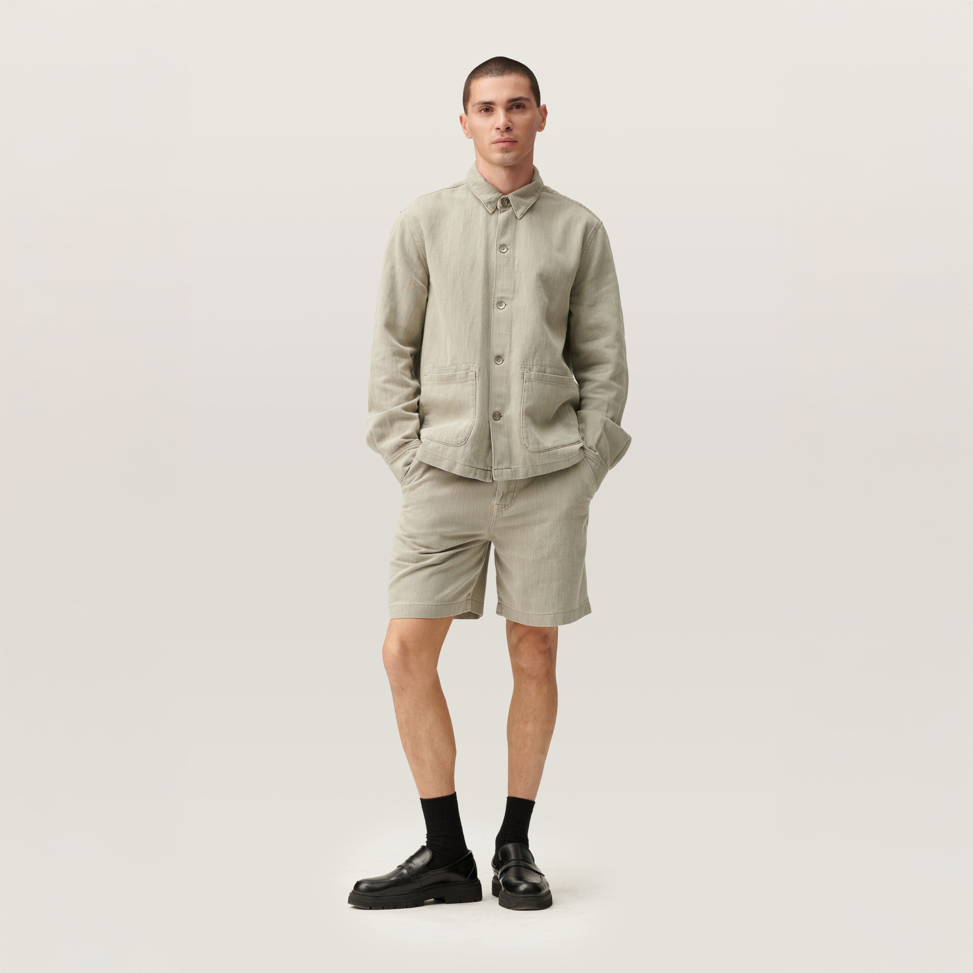 Person trägt Rock Olive SHORTY Shorts aus Lightweight Hemp mit mittlerer Taille und weiterem Schnitt, dazu passendes Hemd aus demselben Stoff.