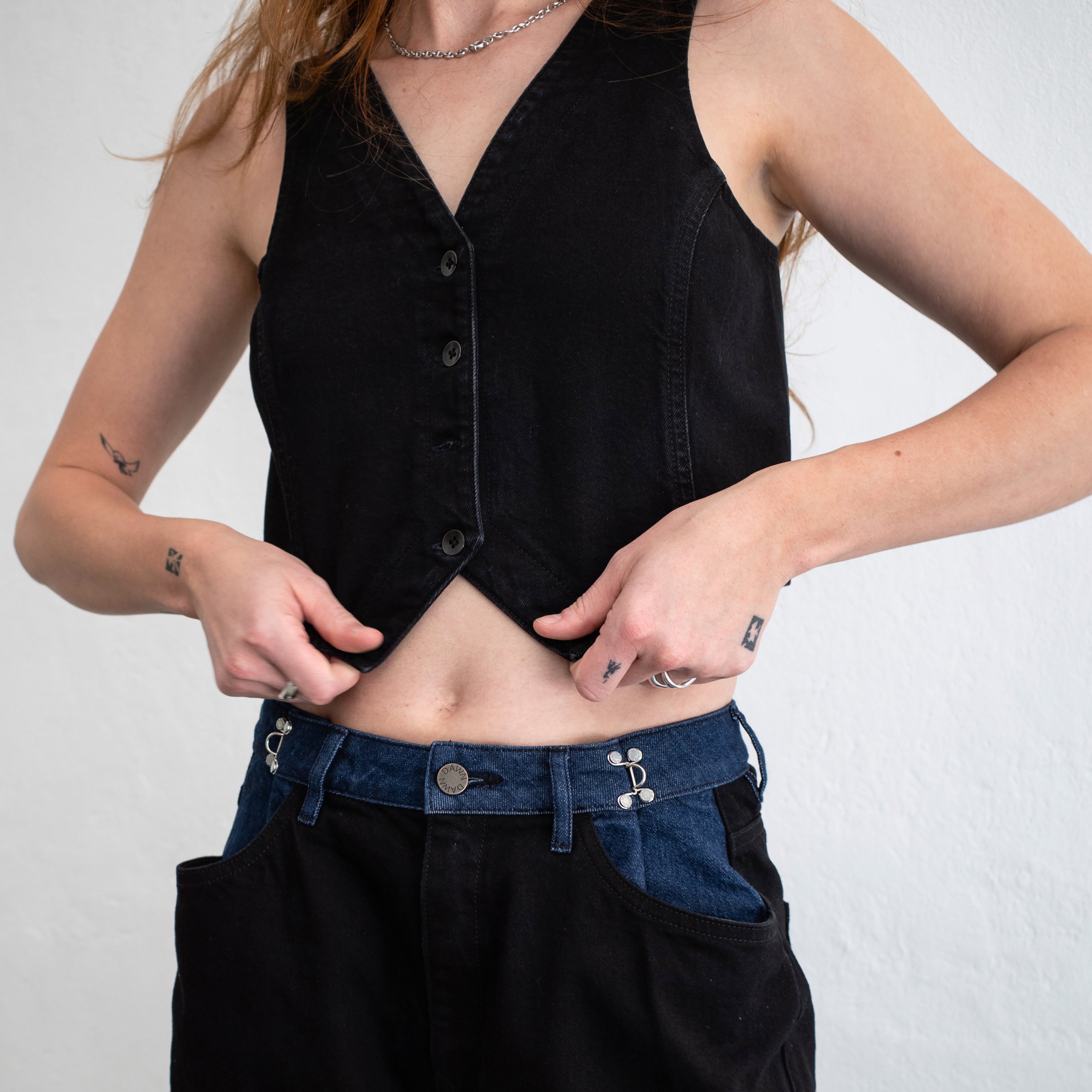 Schwarze, taillierte Denim-Weste mit V-Ausschnitt und Knopfleiste, cropped; Bio-Denim mit leichtem Stretch, am Oberkörper getragen.