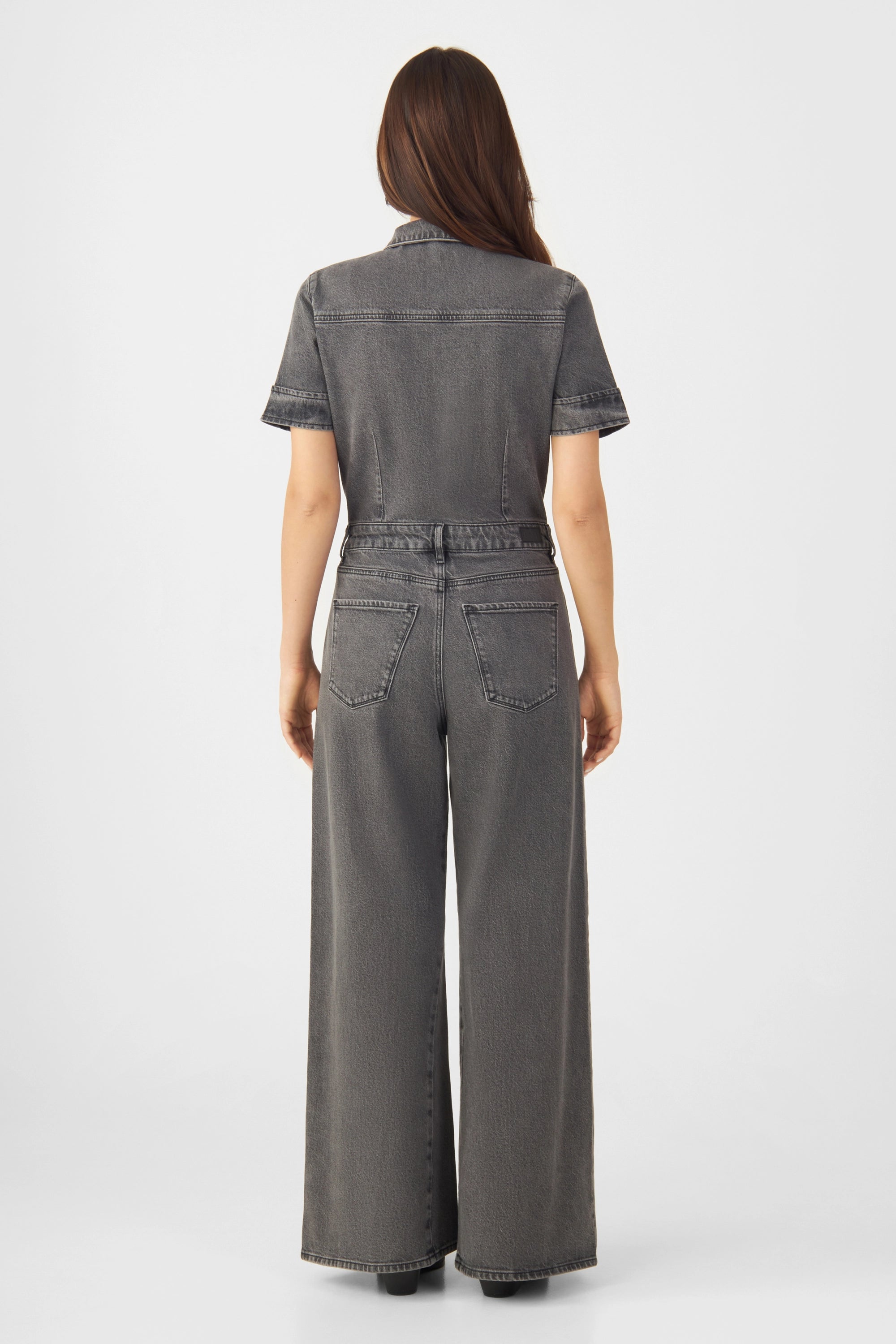 Rückenansicht eines dunkelgrauen Denim-Overalls mit kurzen Ärmeln, weiterem Bein und zwei hinteren Gesäßtaschen.